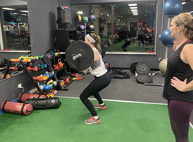 A woman lifting a barbell, while another woman spots for her.