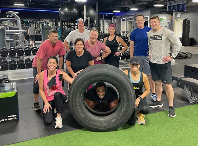 Majestic Fitness members posing indoors with a large tractor tire